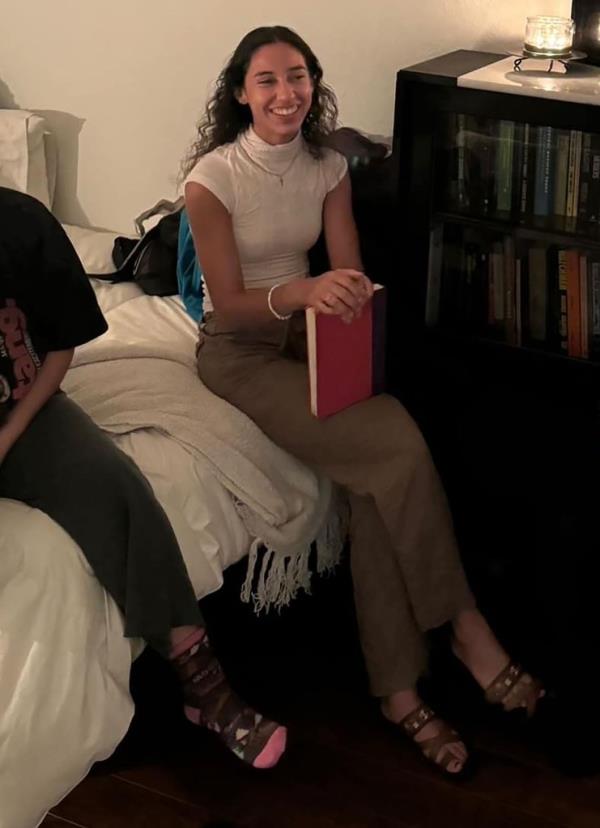 Arielle Valdes sits on a bed laughing while holding a book