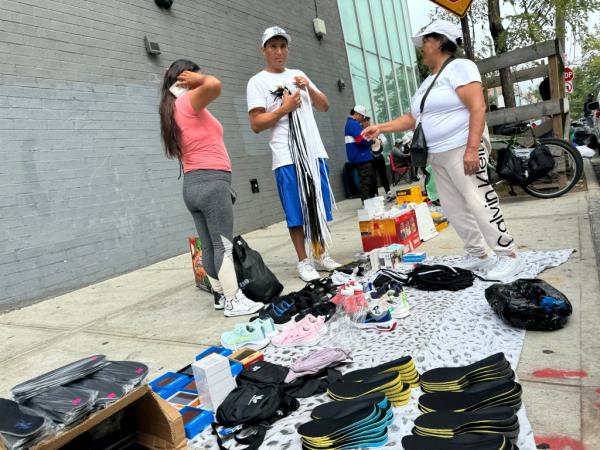 People sell goods on the sidewalk near the intersection of Roosevelt Avenue and 91st Street