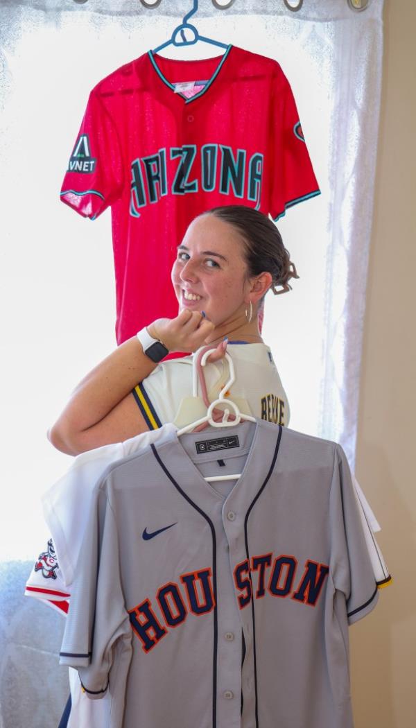 Young woman, Ali Berke, posing with MLB stadium jerseys she has sung the Natio<em></em>nal Anthem at, aspiring to sing at all 30 stadiums