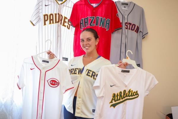 Young woman, Ali Berke, posing with various MLB jerseys she has sung the Natio<em></em>nal Anthem at