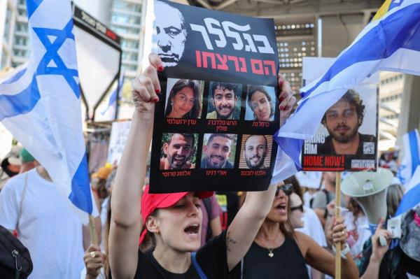 Protester holding up a placard with portraits of six Israeli hostages at a rally in Tel Aviv